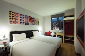 Une chambre d’hôtel avec deux lits, une grande œuvre d’art au mur, une vue sur la ville par la fenêtre et un téléviseur sur le côté droit.
