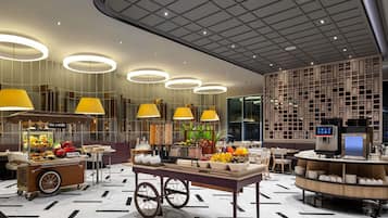 A modern hotel lobby with a food cart, a fruit display, and a seating area with tables and chairs.