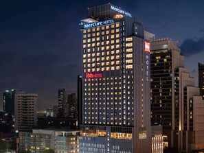 Un grand hôtel, avec de nombreux étages, des fenêtres illuminées et une enseigne bien visible indiquant « MERCURE HOTEL » et « IBIS HOTEL ».