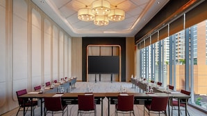 A conference room with a long table, chairs, a projector screen, and large windows with a view of buildings. - Ibis Bangkok Sukhumvit 24 (Bangkok)