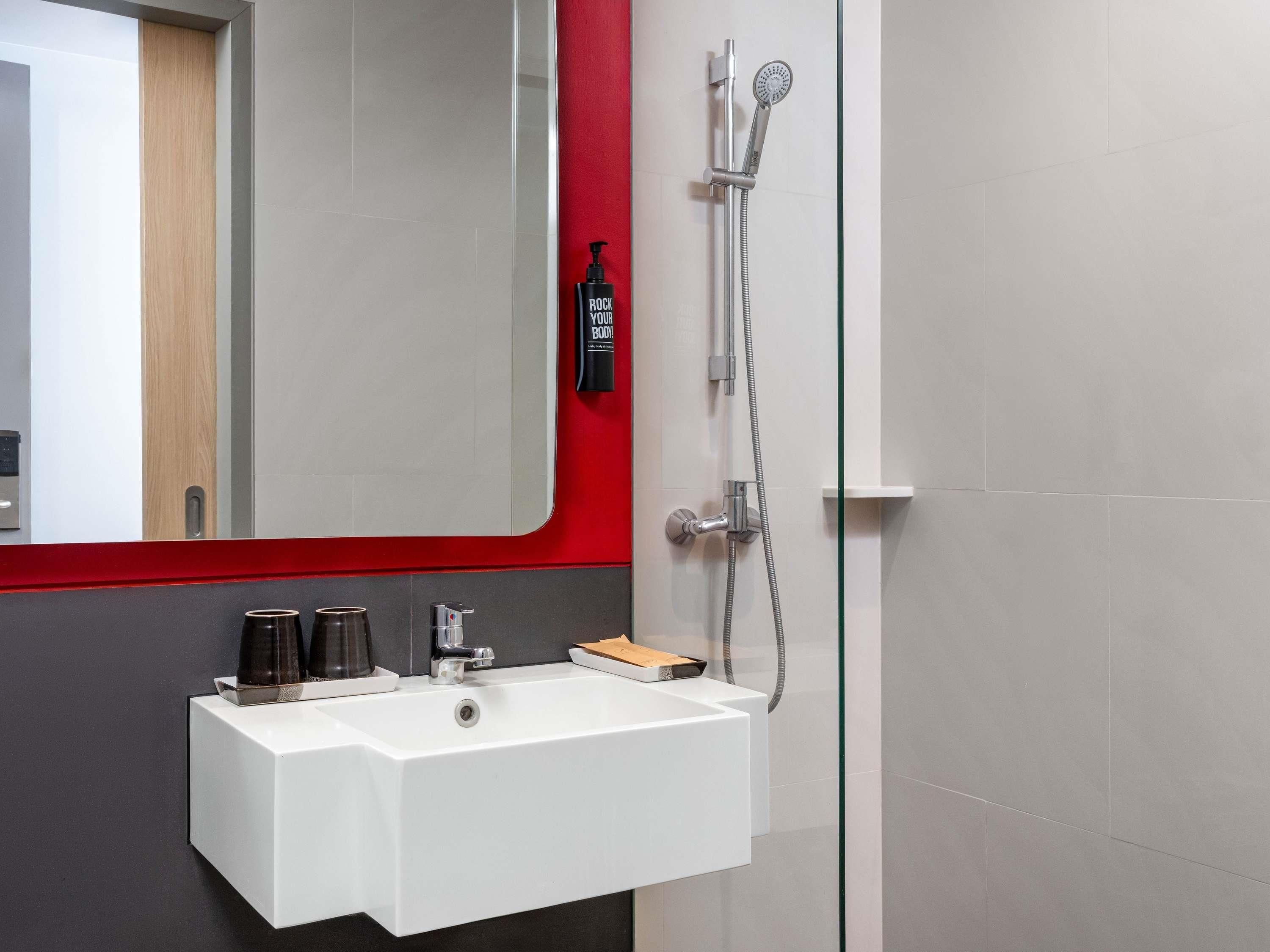 Ein modernes Badezimmer mit einem weißen Waschbecken, einem Spiegel und einer Dusche mit Duschbrause.