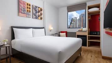 A hotel room with a large bed, a desk, a TV, and a window with a city view.