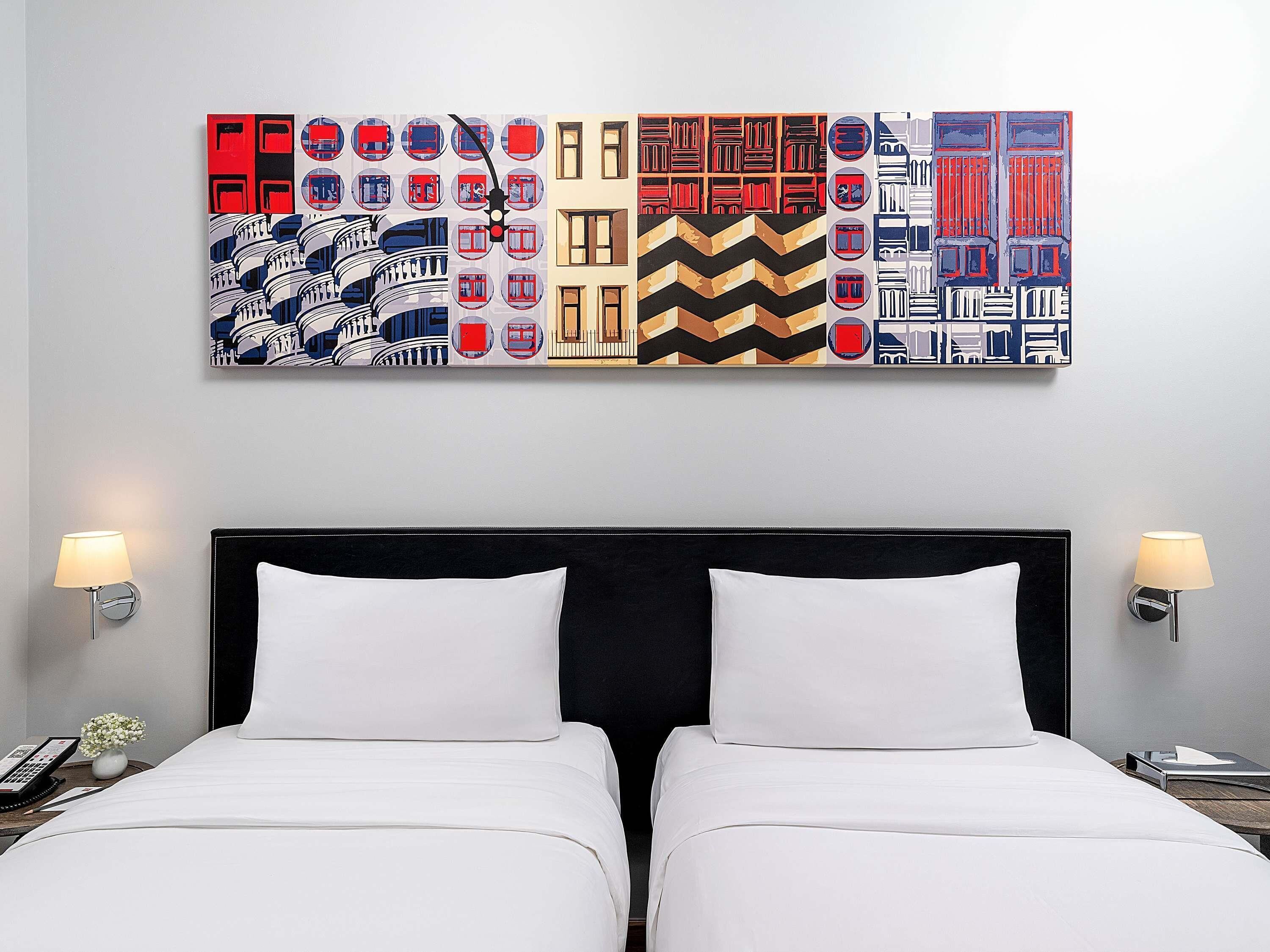 A hotel room with a large abstract painting above the bed, two bedside lamps, and a telephone on the nightstand.