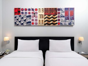 Ein Hotelzimmer mit einem großen, abstrakten Gemälde über dem Bett, zwei Nachttischlampen und einem Telefon auf dem Nachttisch.