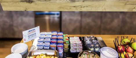 A breakfast buffet with various food items including fruits, pastries, and packaged snacks.