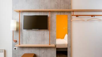 Una habitación moderna con un televisor de pantalla plana montado en una pared gris, un estante de madera debajo y un taburete pequeño.