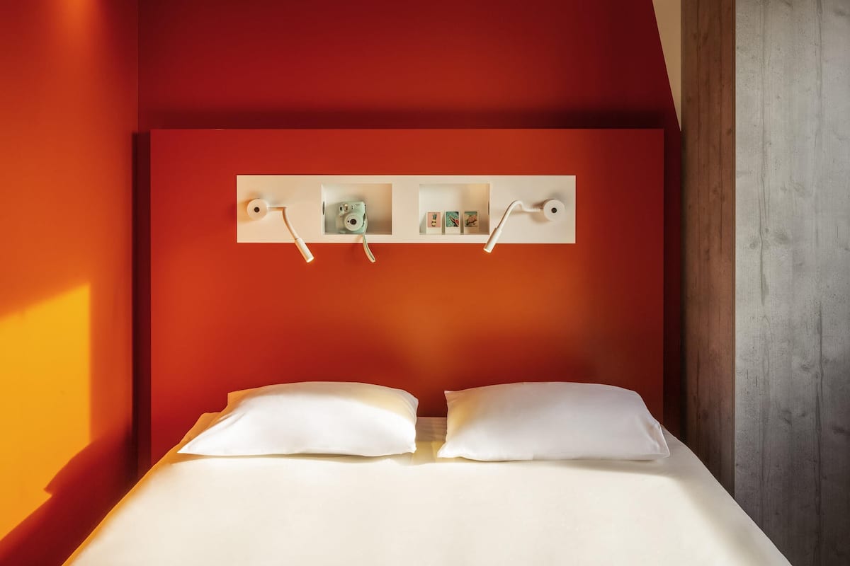 A bed with white bedding, a red wall, and a wooden door.