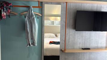 Una habitación de hotel moderna con cabecera gris, un televisor montado en la pared, estante de madera y una cama con mantas de colores.