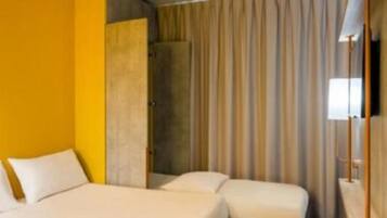 Una habitación de hotel con cama, mesita de noche y cortina.