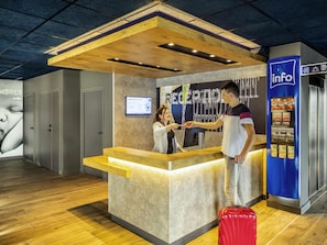 Un comptoir d’accueil avec un plan de travail en bois, un écran numérique et un présentoir d’information bleu.