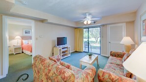 A hotel room with a bed, a TV, a sofa, a coffee table, and a balcony with a view. - Players Club - 2 Bedroom (Hilton Head Island)