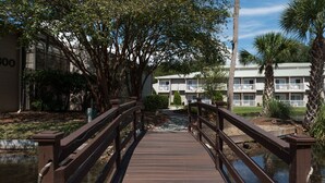 A wooden bridge over a small water body, leading to a building with balconies and a white exterior. - Players Club - 2 Bedroom (Hilton Head Island)