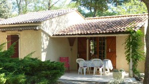 A house with a tiled roof, a covered porch with a table and chairs, and a red door. - Your house in pines and green oaks (Uchaux massif). (Mornas)