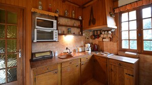A wooden cabin kitchen with a built-in microwave, wooden cabinets, a sink, and a window with a view of trees. - Your house in pines and green oaks (Uchaux massif). (Mornas)