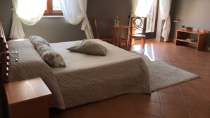 A bedroom with a bed, bedside tables, a chair, a small table, and a TV on the wall. - Tenuta Re Ferdinando (Santa Maria Capua Vetere)