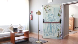 A room with a sofa, a small wooden table, a floor lamp, a decorative glass door with artwork, and a fire extinguisher on the wall. - Tenuta Re Ferdinando (Santa Maria Capua Vetere)