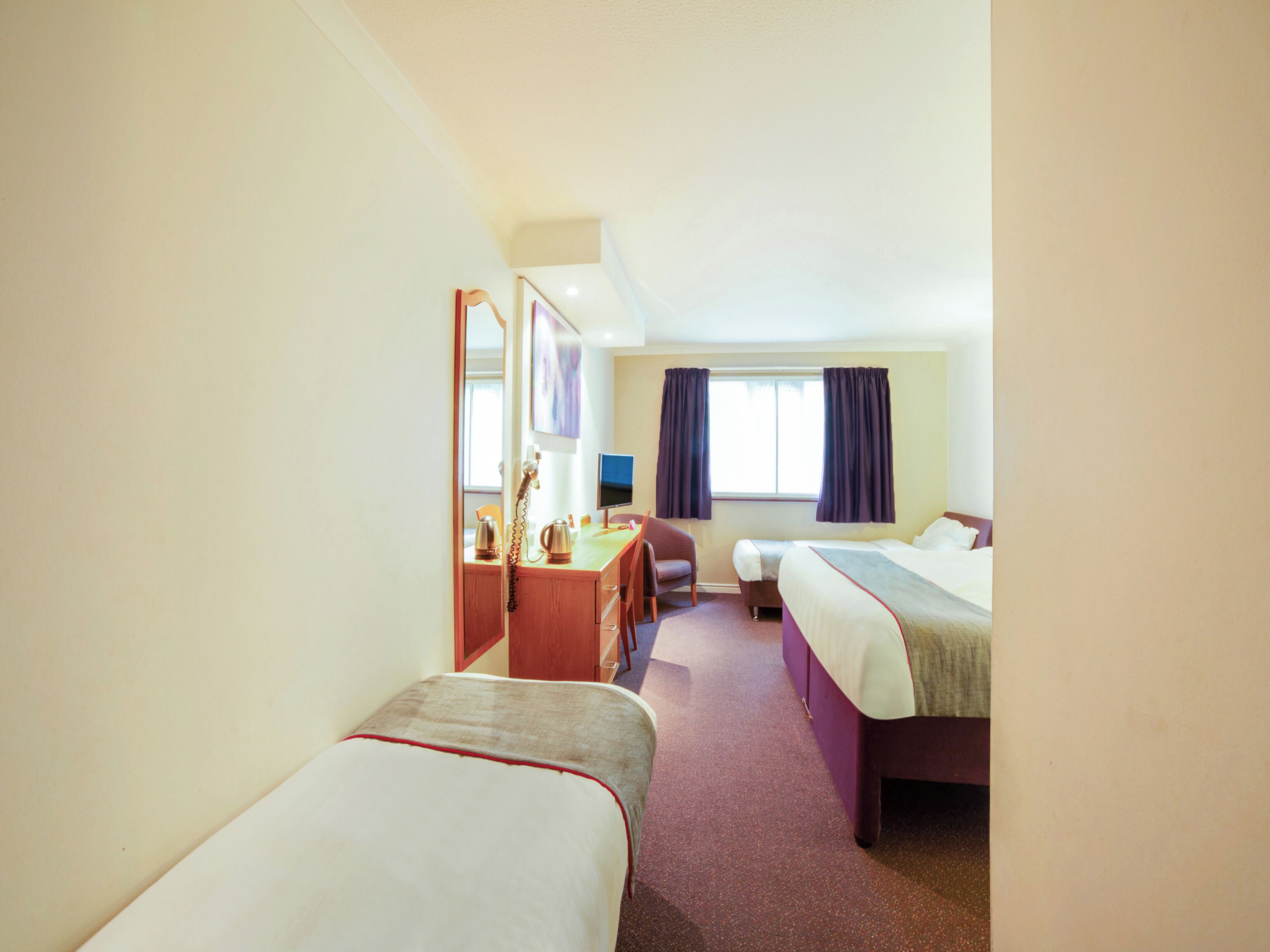 Ein Hotelzimmer mit zwei Einzelbetten, einem Schreibtisch mit Stuhl, einem Telefon und einem Fenster mit Vorhängen.