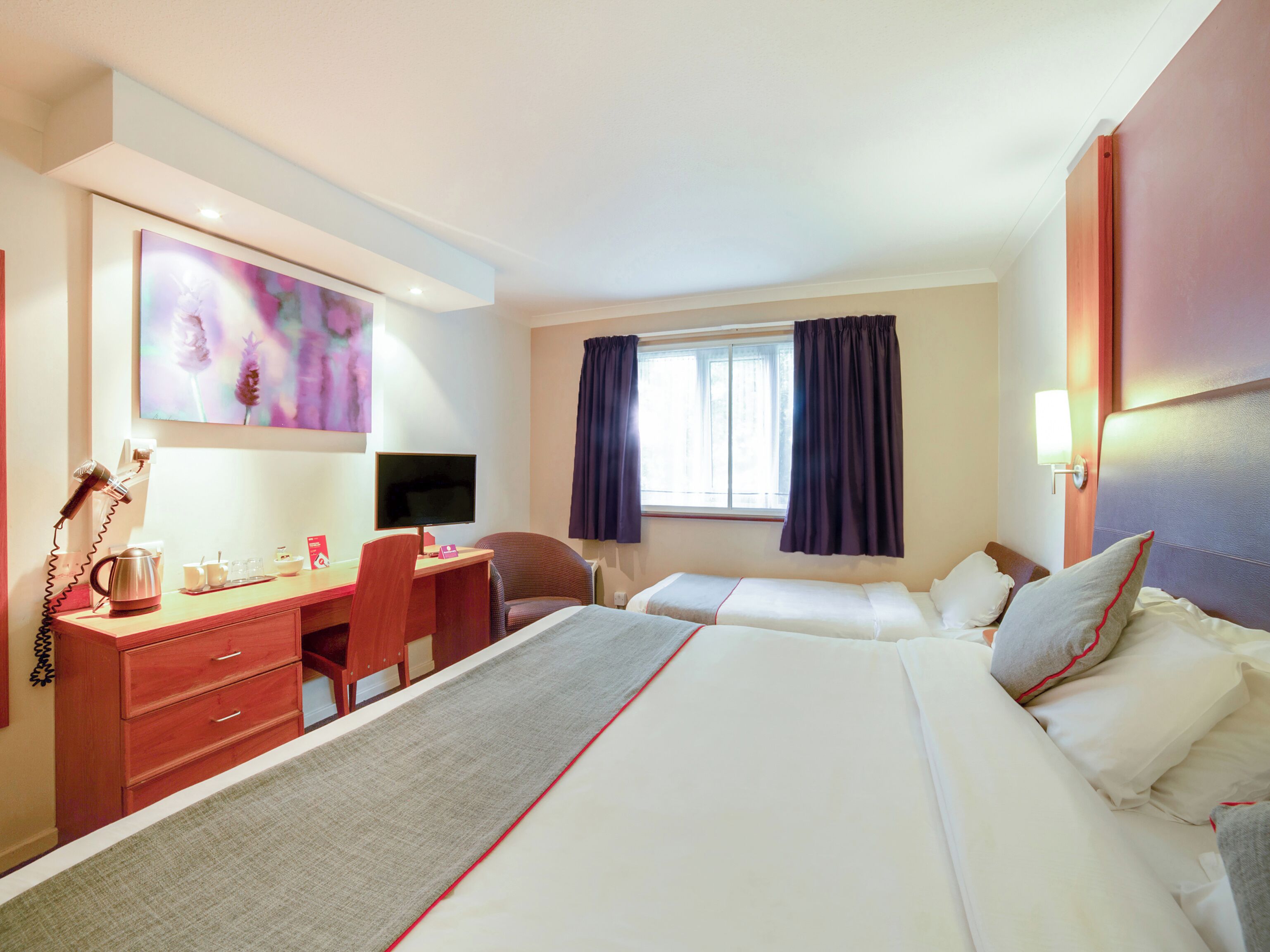 A hotel room with a bed, a desk, a chair, a TV, and a painting on the wall.