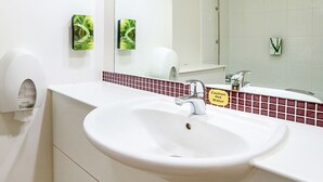 Un baño con un lavamanos blanco, un espejo, un secador de manos y un letrero de precaución sobre agua caliente.