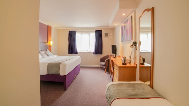 Habitación de hotel con cama, escritorio, silla, lámpara de escritorio, televisor y ventana con cortinas.