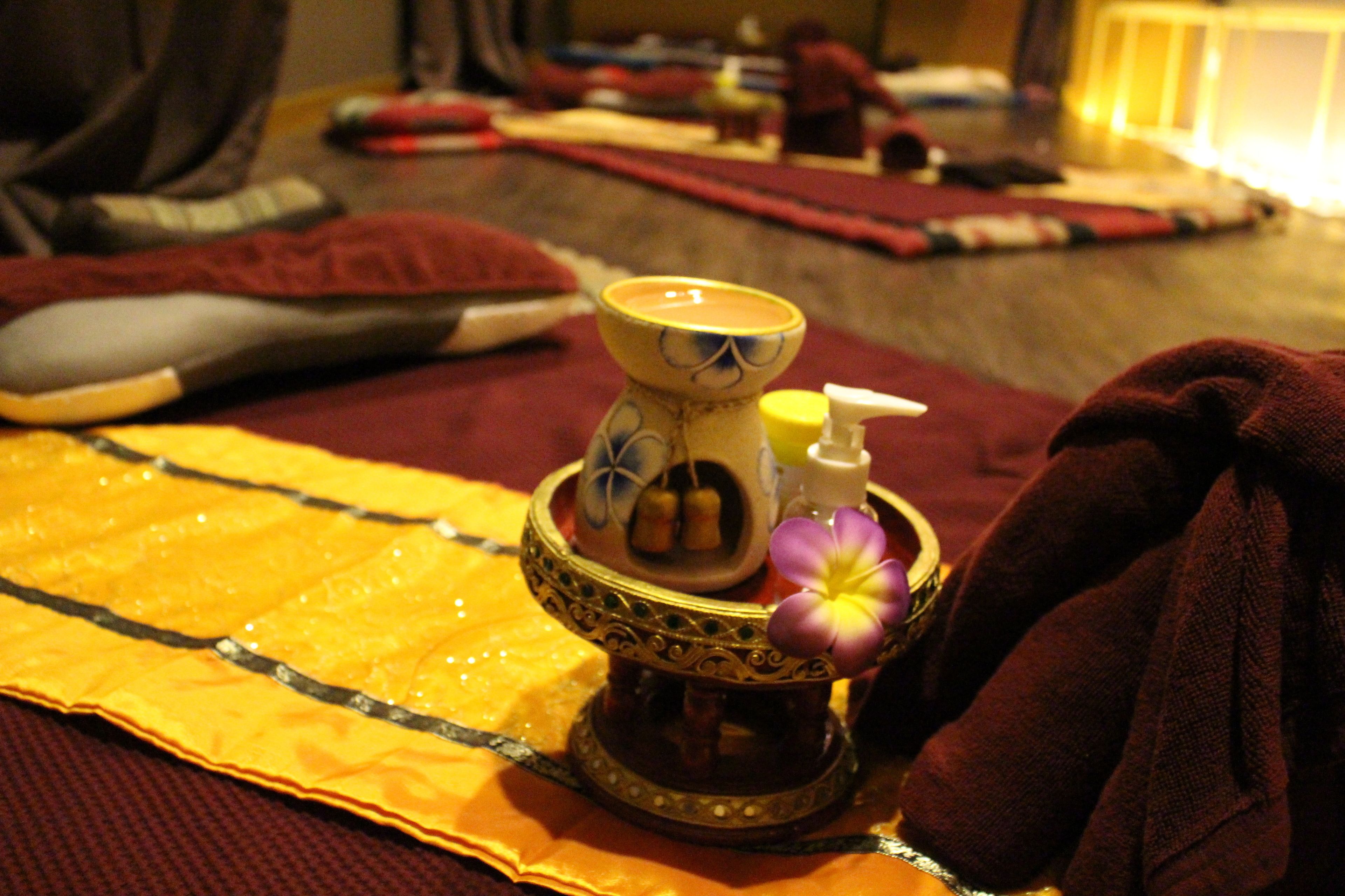 A room with a bed covered in a yellow blanket, a red blanket, and a brown blanket. There is a small table with a decorative item on it.