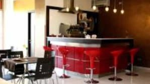 A modern kitchen with red bar stools, a dining area with a table and chairs, and a ceiling with pendant lights. - Tea Palace Hotel (Casapulla)
