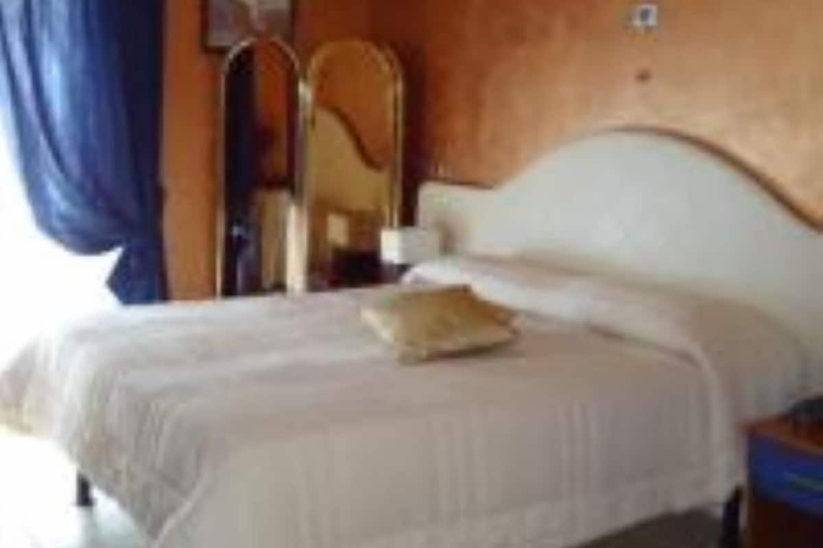 A hotel room with a bed, a nightstand, a mirror, and a window with curtains.