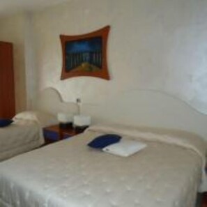 Una habitación de hotel con dos camas, una mesita de noche, una lámpara y un cuadro en la pared.