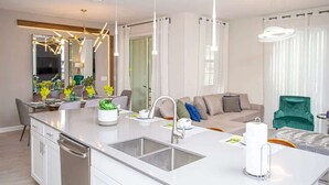Eine moderne Küche mit einer zentralen Kochinsel, einem Essbereich mit Tisch und Stühlen, einer Couch und einem grünen Sessel.