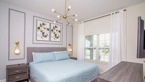 Ein Schlafzimmer mit Bett, Nachttischen, Schreibtisch, einem modernen Kronleuchter und Bildern an der Wand.