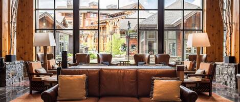 Eine Lobby mit einer Ledersofa, mehreren Sesseln, einem Couchtisch und einem großen Fenster mit Blick auf Gebäude und eine Steinmauer.