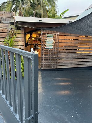 A wooden fence with a gate leading to a building with a signboard listing amenities like 'The Beach' and 'Cocktail Party'.
