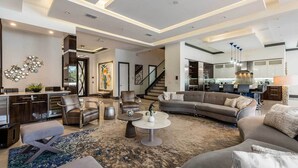 Ein modernes Wohnzimmer mit einer Couch, Sesseln und einem Couchtisch. Im Hintergrund ist eine Küche mit Essbereich erkennbar.