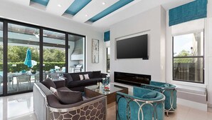 A modern living room with a sofa, coffee table, and TV. There is a large window and a balcony with outdoor furniture. - Grand Villa Near Disney w Game RM, Theater, Ice Princess & Wizard BRs & Spa Pool (Four Corners)