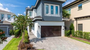 A modern two-story house with a garage, surrounded by well-maintained landscaping and a clear blue sky. - Grand Villa Near Disney w Game RM, Theater, Ice Princess & Wizard BRs & Spa Pool (Four Corners)