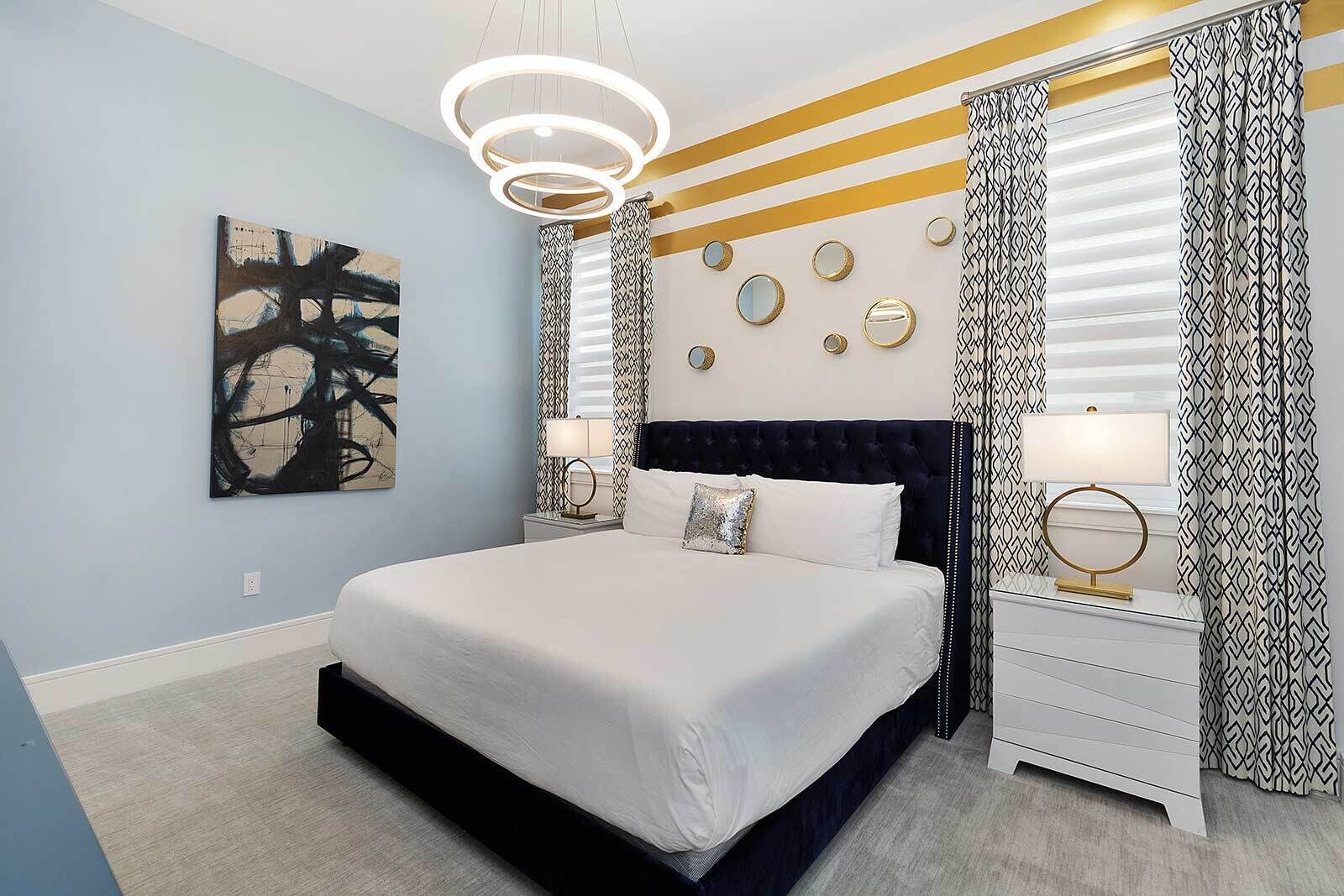 A modern bedroom with a large bed, a bedside table with a lamp, a wall-mounted mirror, and a geometric-patterned curtain.