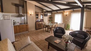 Ein geräumiger Wohnbereich mit Esstisch, zwei Sofas und Couchtisch. Im Hintergrund ist eine Küche mit Holzausbau und integriertem Backofen zu sehen.