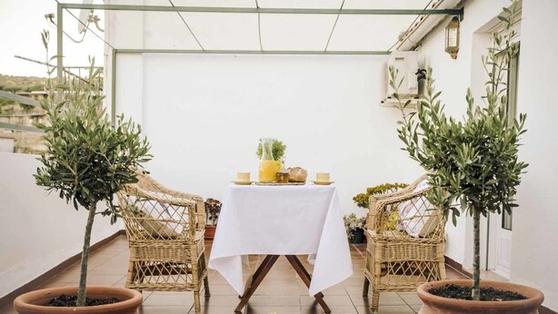 Eine Terrasse mit Tisch für zwei Personen, umgeben von Korbstühlen und Topfpflanzen.