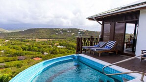 Ein Pool mit Blick auf eine üppige Landschaft, eine überdachte Terrasse mit Liegestühlen und ein Holzdeck.