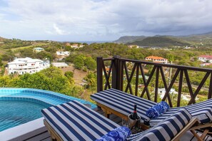 A poolside area with lounge chairs, a bottle of champagne, and a view of a residential area with houses and hills.
