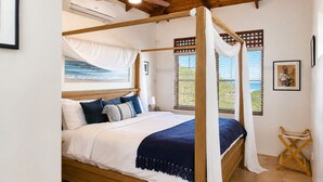 Ein Himmelsbett mit Baldachin, Holzbalken, Deckenventilator und Blick auf den Strand.