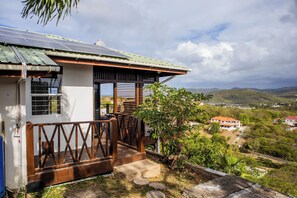 Ein Haus mit Solardach, einer Holzterrasse und Blick auf eine hügelige Landschaft.