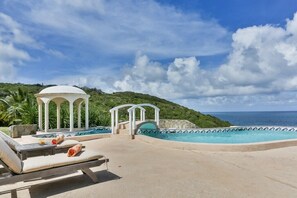 A pool area with lounge chairs and a gazebo, overlooking a hillside and the ocean.