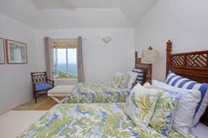 A bedroom with two beds, a window with a view of the sea, a chair, and a decorative wall piece.