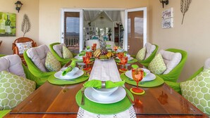 Een eettafel gedekt met groene placemats, witte servetten en een fruitstuk als decoratie.