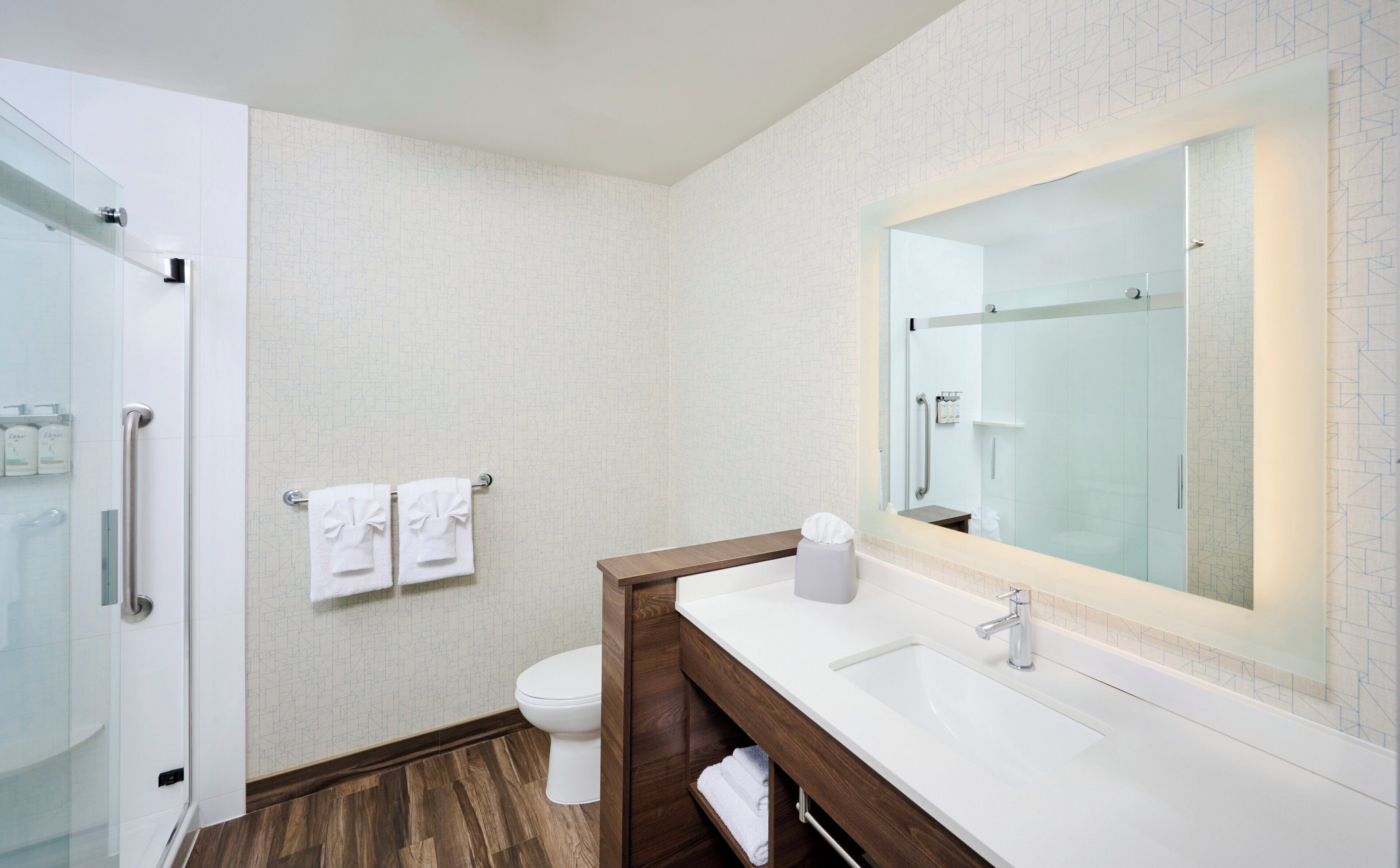 Un baño moderno con cabina de ducha de vidrio, inodoro blanco y tocador de madera con un espejo grande.