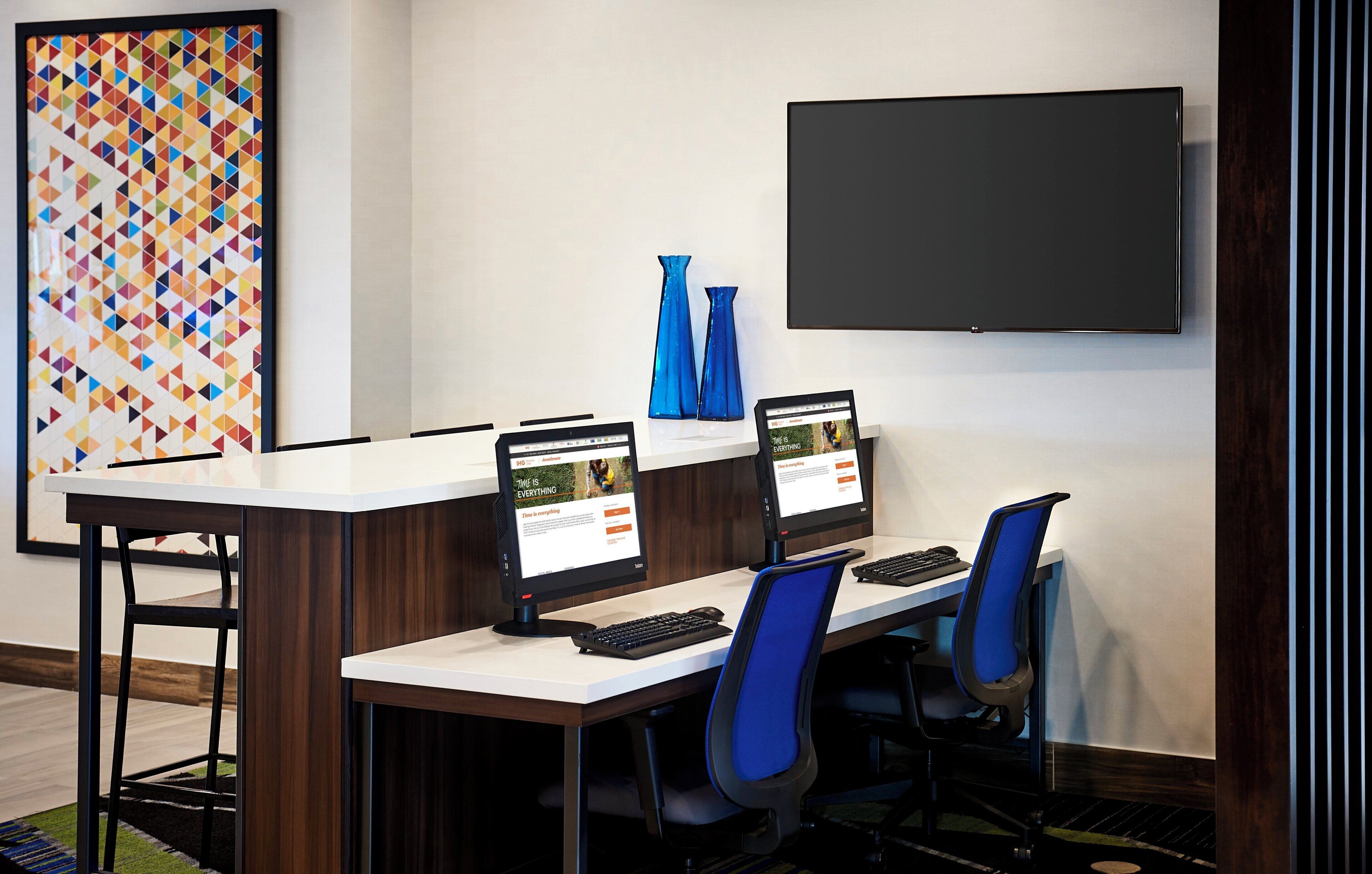A modern office space with a long table, two chairs, two computers, and a large framed artwork on the wall.
