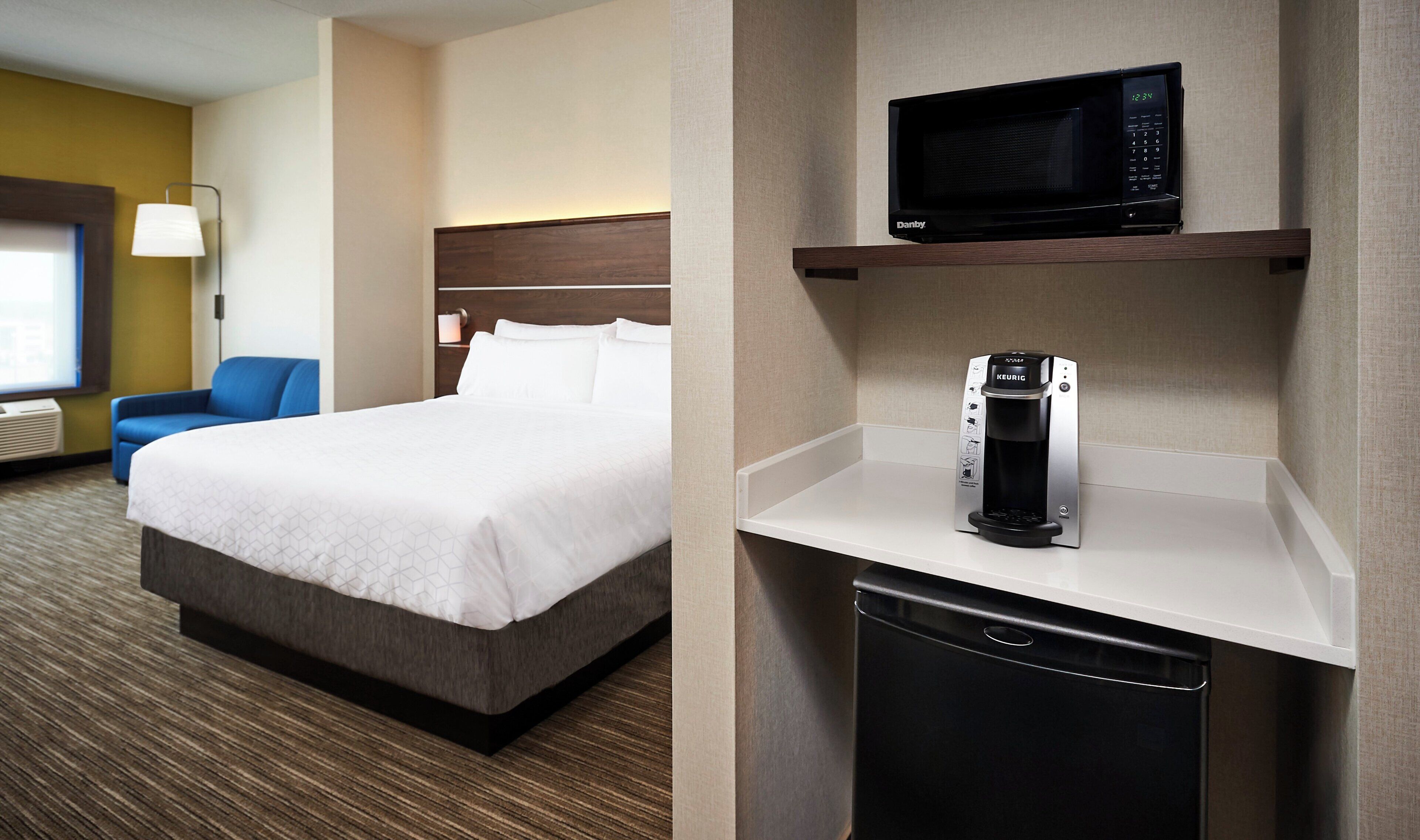 A hotel room with a bed, a blue chair, a microwave, and a coffee maker.