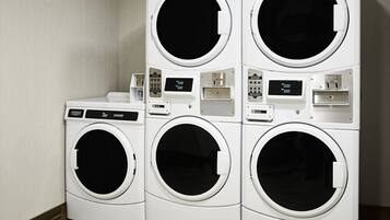 A set of four stacked front-loading washing machines in a room with wooden flooring and light-colored walls.