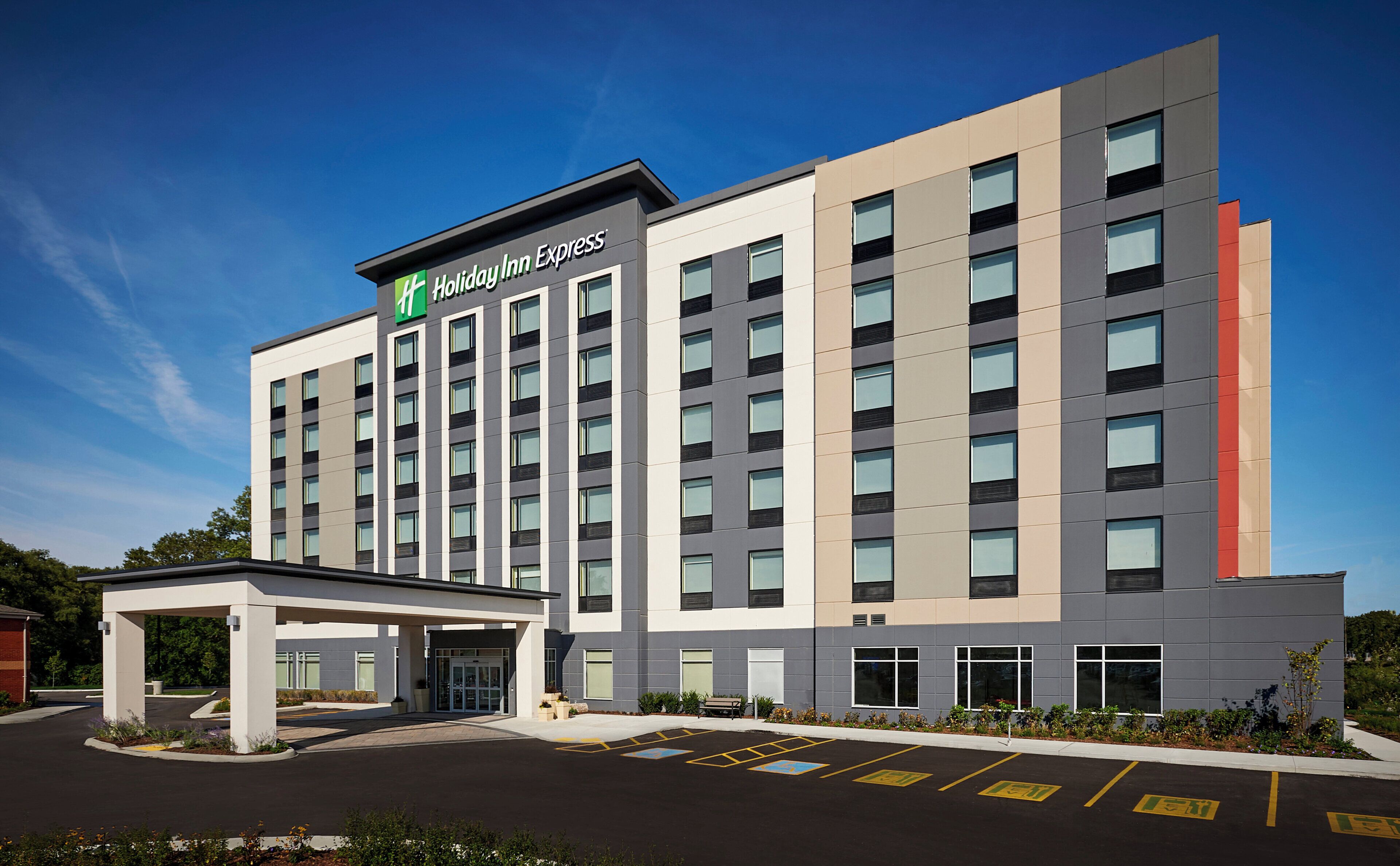 Un hotel Holiday Inn Express con fachada moderna, un acceso cubierto y un estacionamiento con espacios para discapacitados.